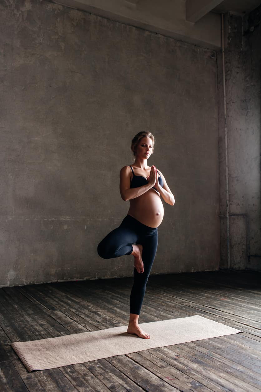 Femme enceinte pratiquant une posture de yoga d’équilibre, mettant en avant l’activité physique pendant la grossesse.